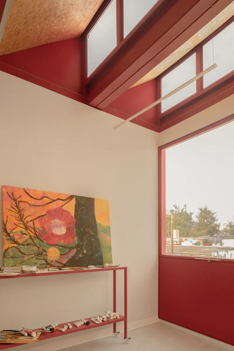 Corner detail showing red metal framing around plywood ceiling panel and window overlooking trees