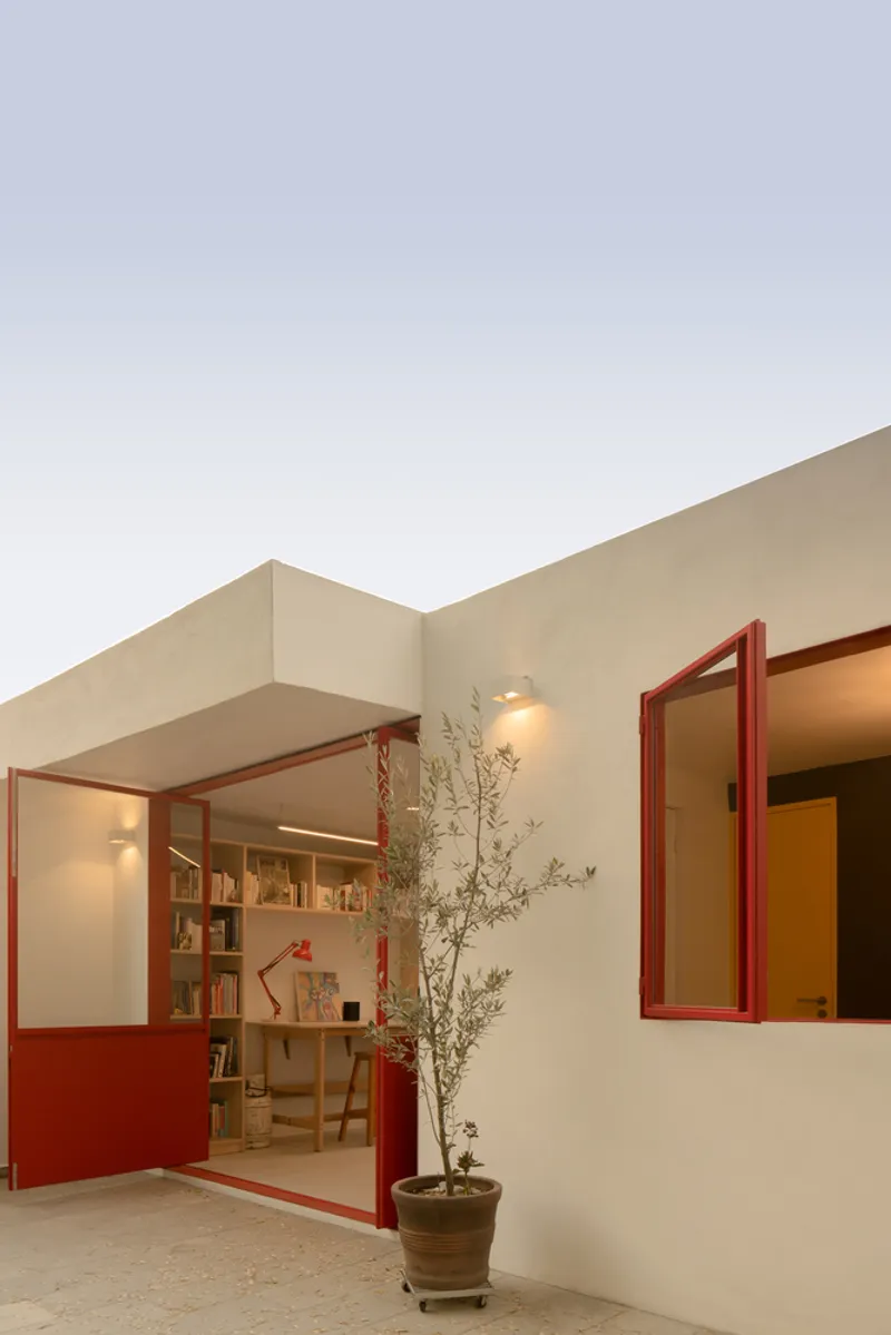Exterior courtyard with red steel framed windows opening onto a study at dusk