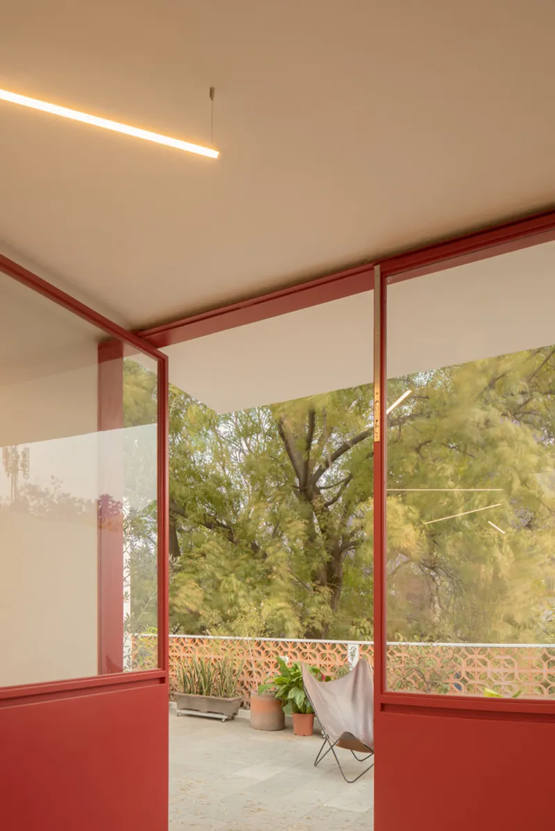View through red steel framed openings to a terrace with potted plants and trees beyond