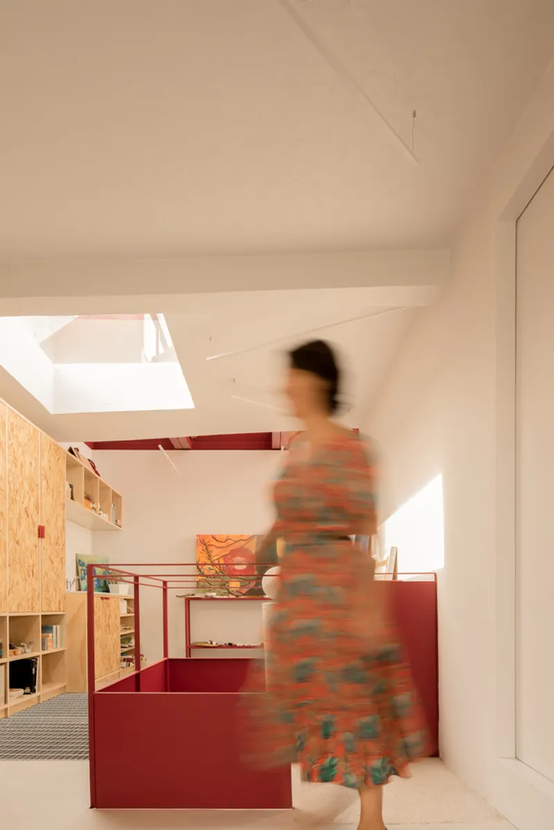 Interior hallway with a figure in motion passing red steel partitions and plywood shelving