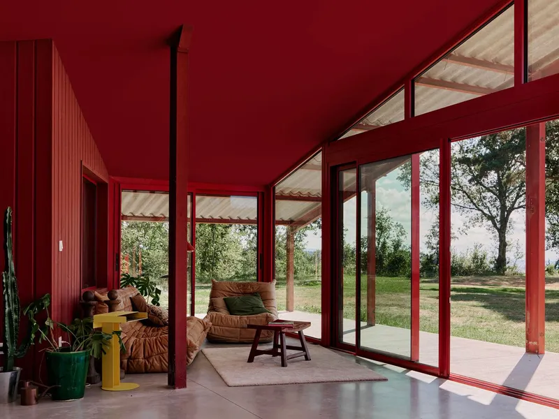 Interior living area with red steel columns and full-height glazing opening to a lawn under sloped timber soffit