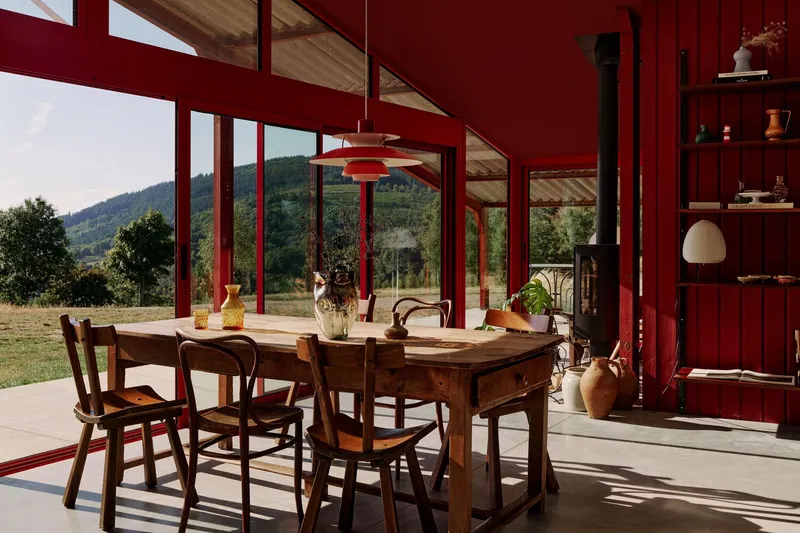 Dining table beneath a suspended pendant light framed by red steel columns with mountain views beyond
