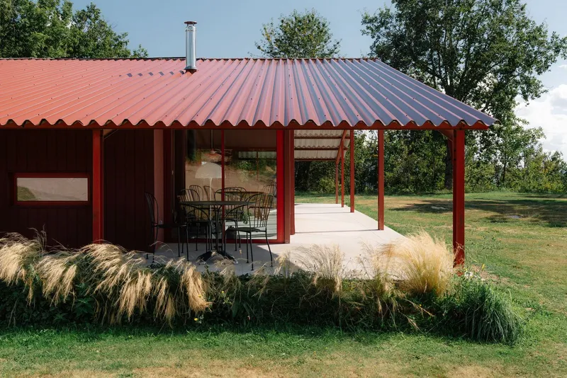Corner of the corrugated metal roof extending over a porch with ornamental grasses in the foreground