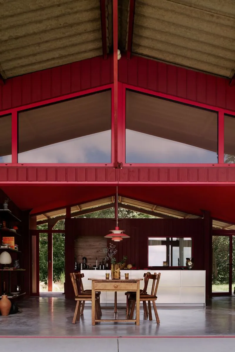 Double-height interior with red painted timber walls and exposed gable ceiling above the dining area