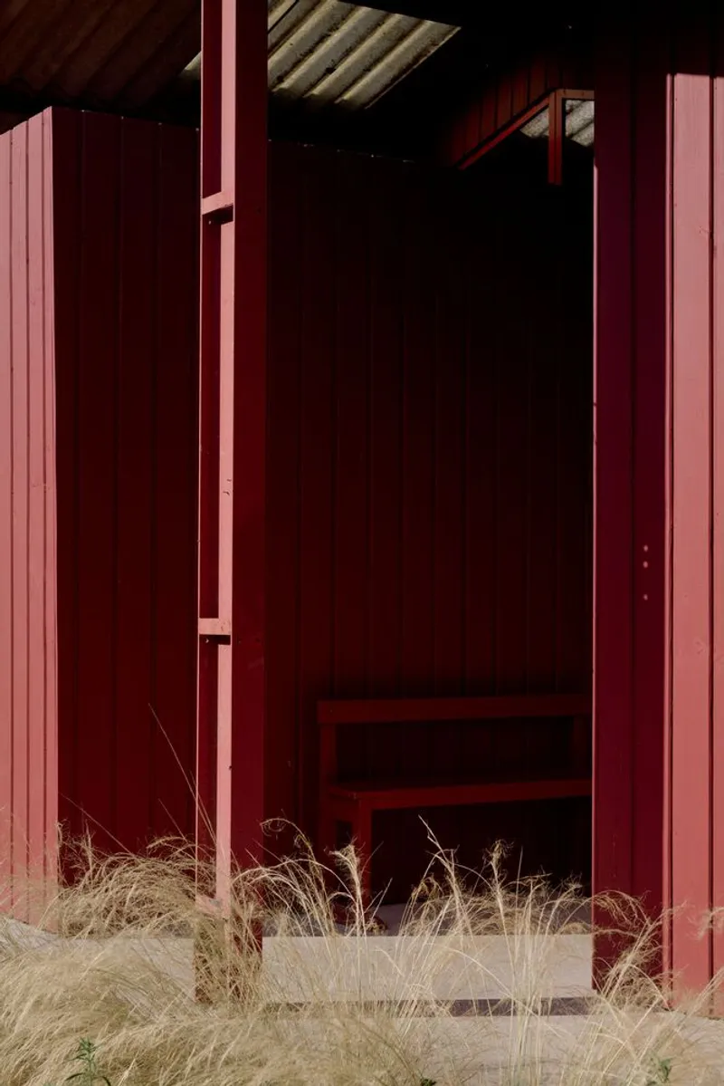 Open doorway in red corrugated metal cladding with dry grasses at the threshold