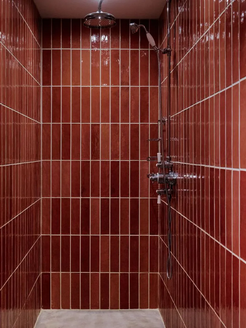 Shower enclosure lined with vertical terracotta tiles and white grout grid with chrome fixtures
