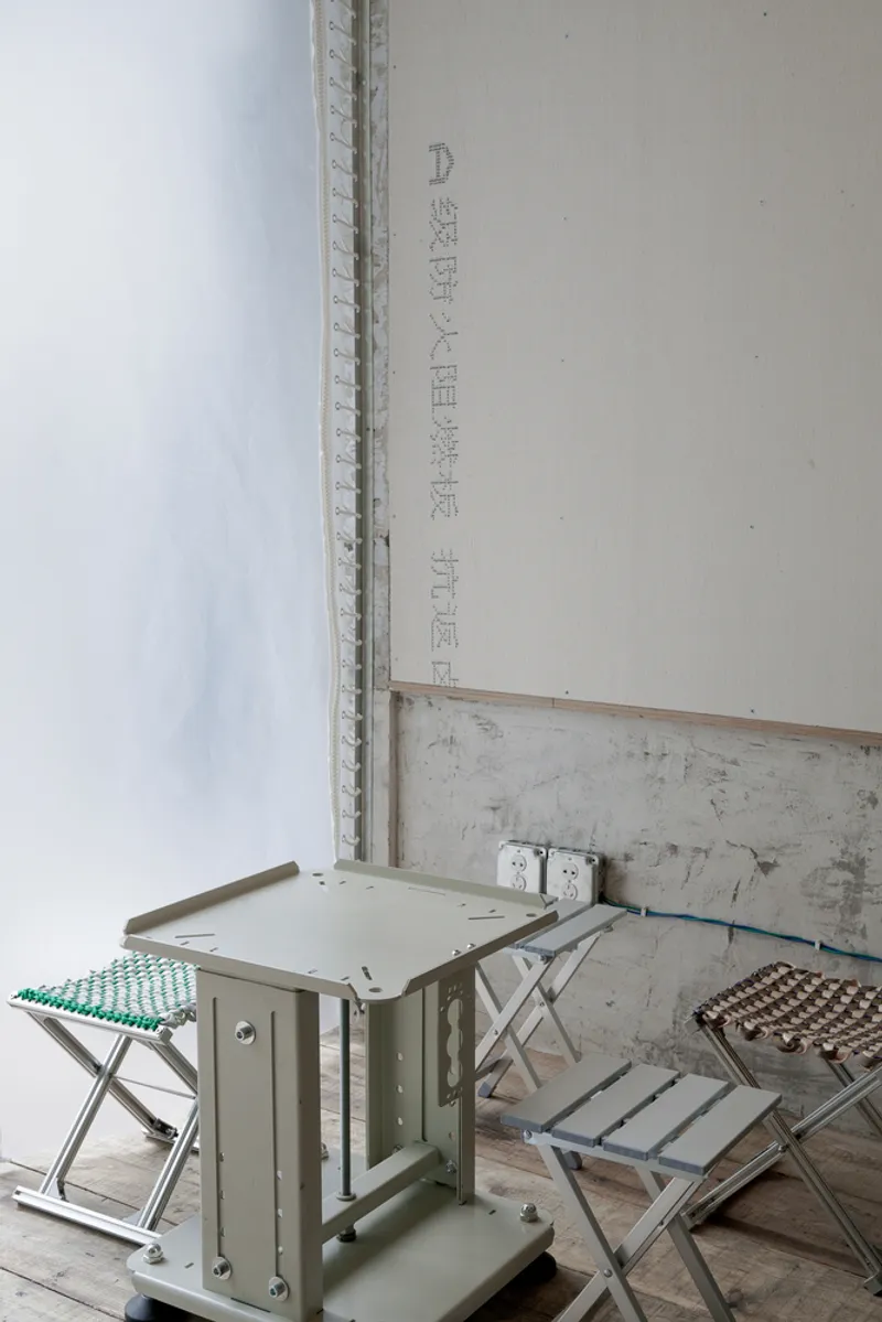 Corner of a room with plywood walls and folding metal stools with perforated seats