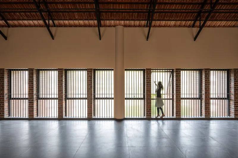 Interior corridor with brick-framed vertical slatted windows and exposed timber ceiling structure as a person walks past
