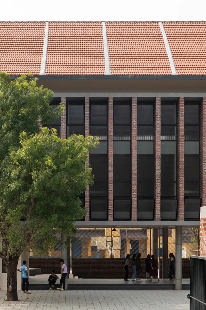 Street view of the brick facade with vertical window bays beneath a terracotta tile roof with a tree in front