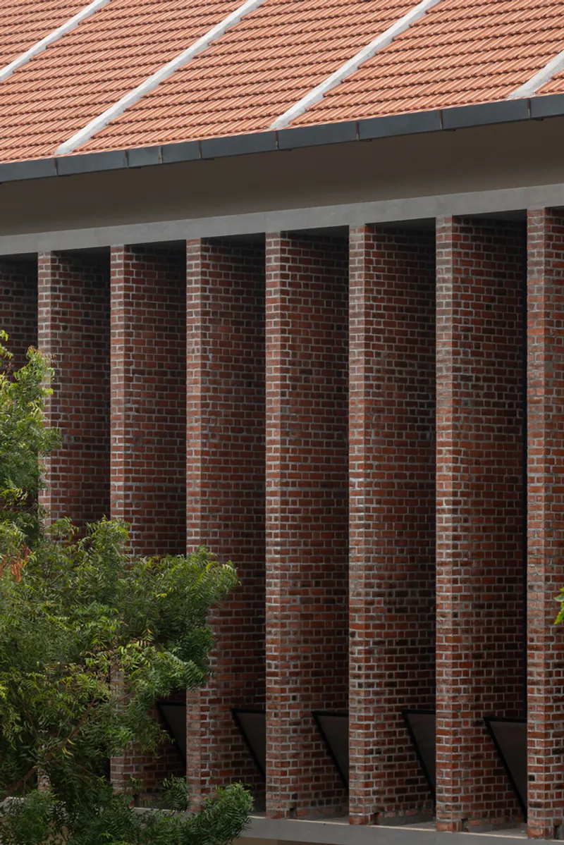 Close-up of the rhythmic brick piers with recessed vertical window openings beneath the terracotta tile eaves
