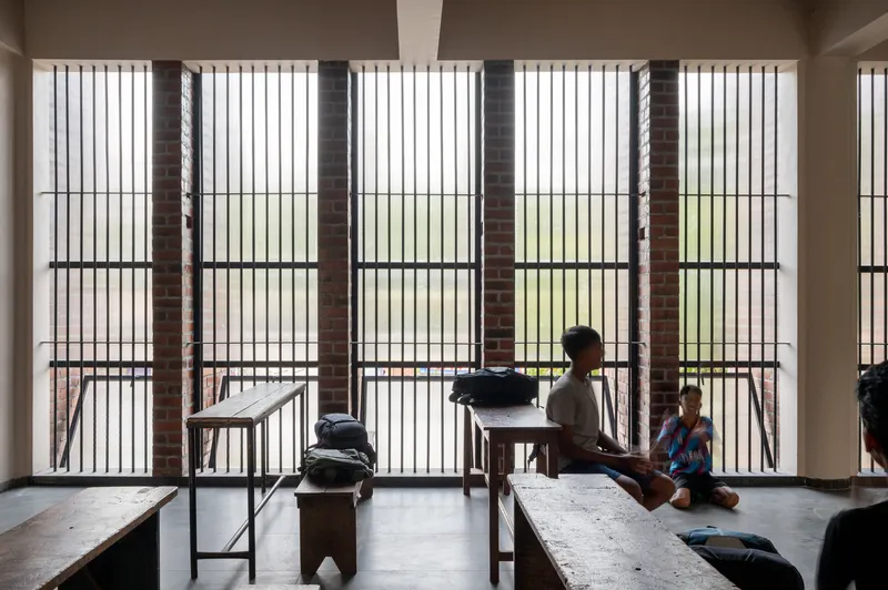 Interior hall with brick screen wall and students seated on benches in filtered daylight