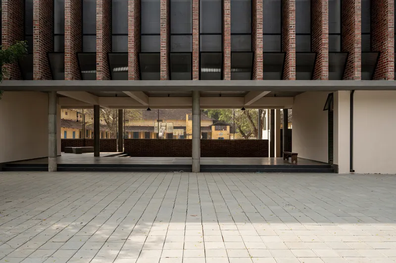 Covered ground floor loggia with concrete columns and brick facade above a paved courtyard