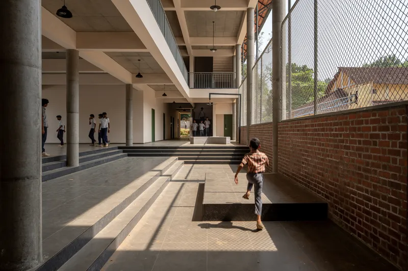 Circulation zone with steps casting shadows as a child runs past brick wall