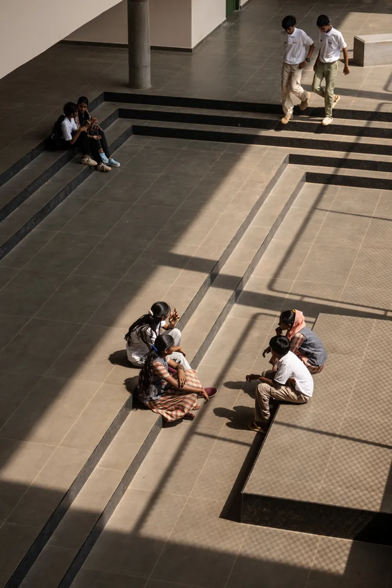 Top-down view of a tiled courtyard with stepped seating and visitors casting long afternoon shadows