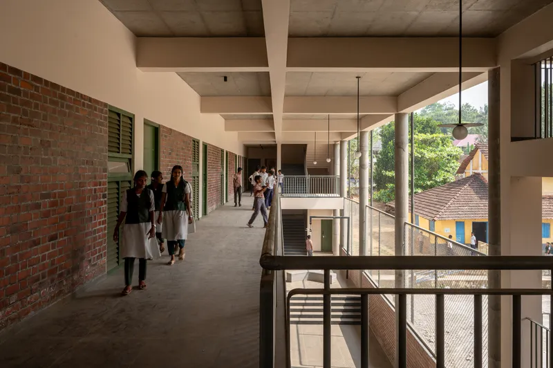 Open corridor with exposed concrete ceiling beams, brick wall and green shutters, students walking