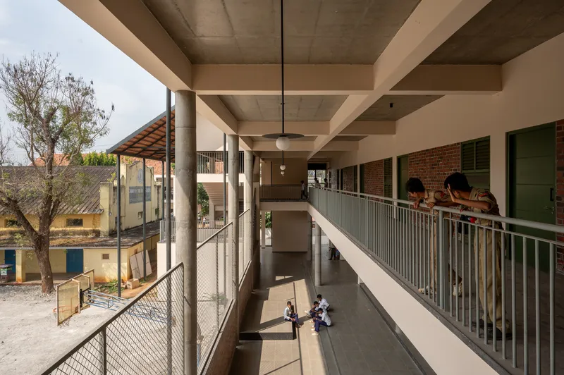 Double-height circulation corridor with concrete ceiling coffers and metal mesh railings overlooking a courtyard