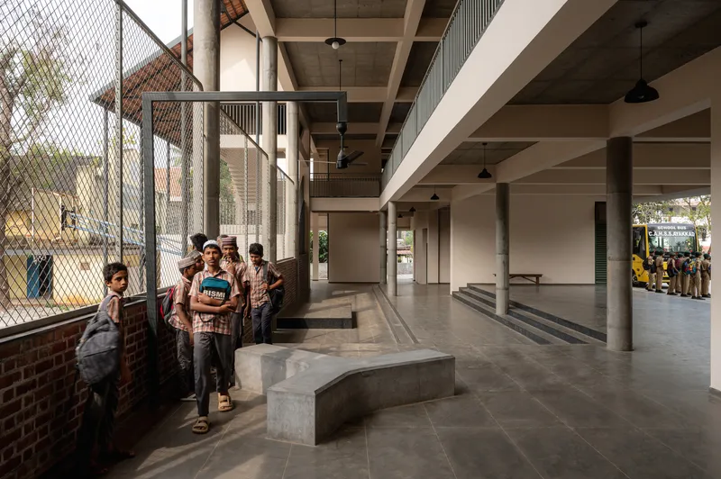 Ground-floor hall with concrete benches, cylindrical columns and mesh-fenced courtyard with students gathered