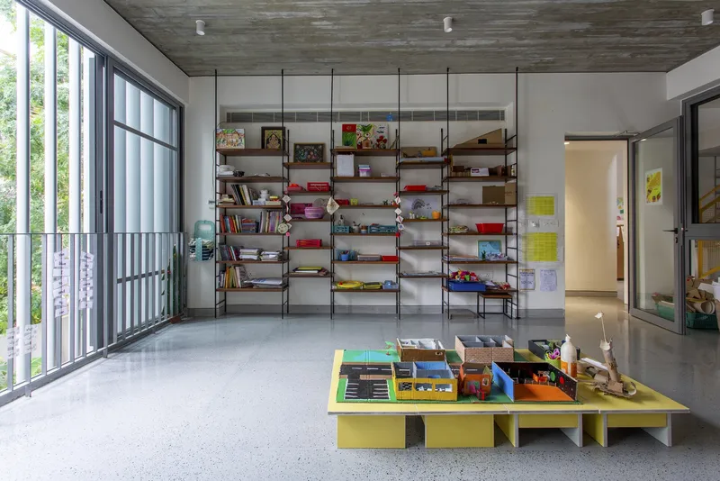 Interior room with wall-mounted shelving system and yellow low table beneath a board-formed concrete ceiling