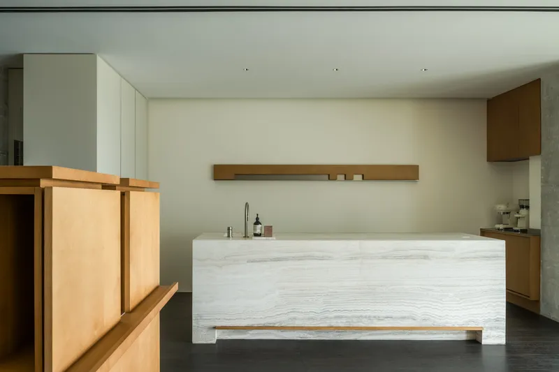 Freestanding counter clad in pale veined wood with timber shelf and cabinetry