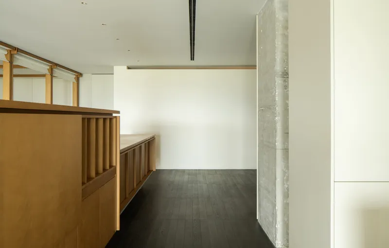 Board-formed concrete column beside built-in timber bench and storage along white wall