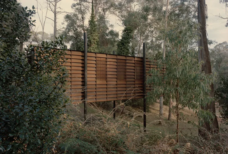 Horizontal timber louvres suspended on steel posts in the sloping wooded landscape