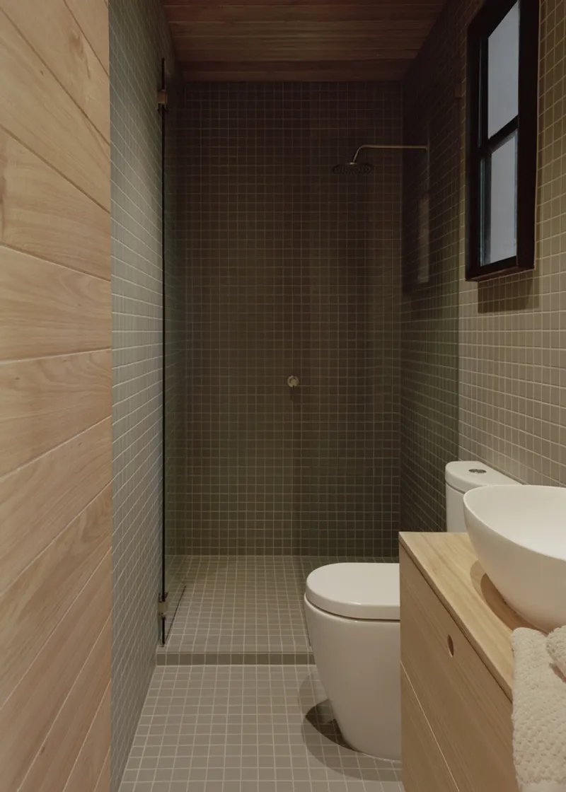 Bathroom with olive mosaic tile shower enclosure and timber-clad walls under a dark timber ceiling