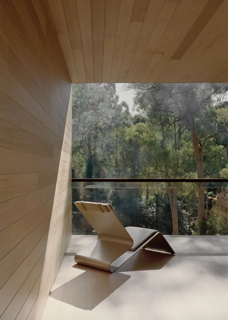 Covered terrace with folded lounge chair overlooking dense eucalyptus canopy through cable railing