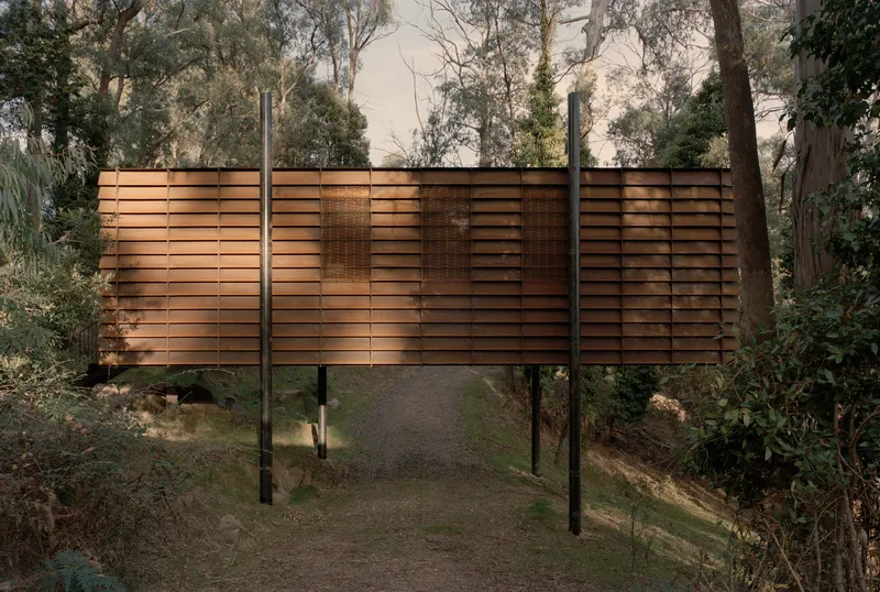 Elevated timber screen walkway on steel columns spanning a gravel path through the bushland