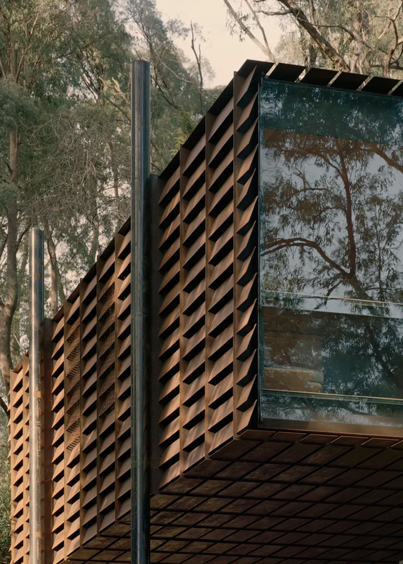 Corner detail showing diagonal timber battens and steel column beside glazed facade reflecting surrounding trees