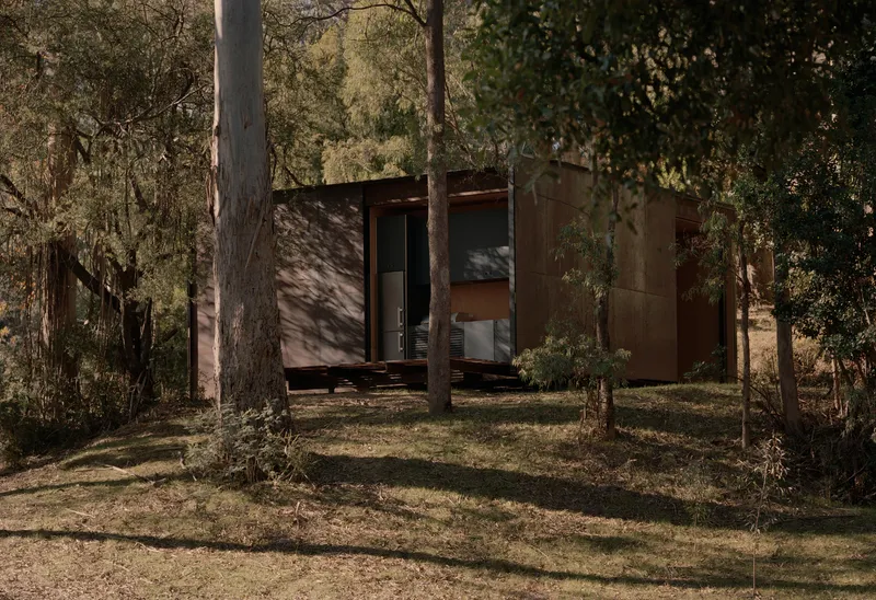 Weathered steel box volume with open doorway and glazing set within a clearing of tall eucalypts