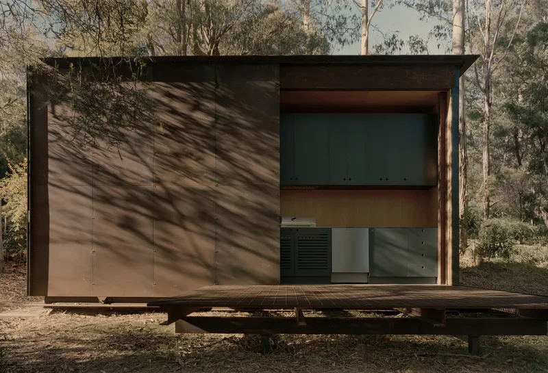 Front facade showing steel panels and timber cladding with tree shadows cast across the surface at dusk