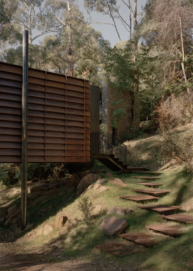 Cantilevered timber louvre volume above outdoor stair treads set into a sloping grassy hillside