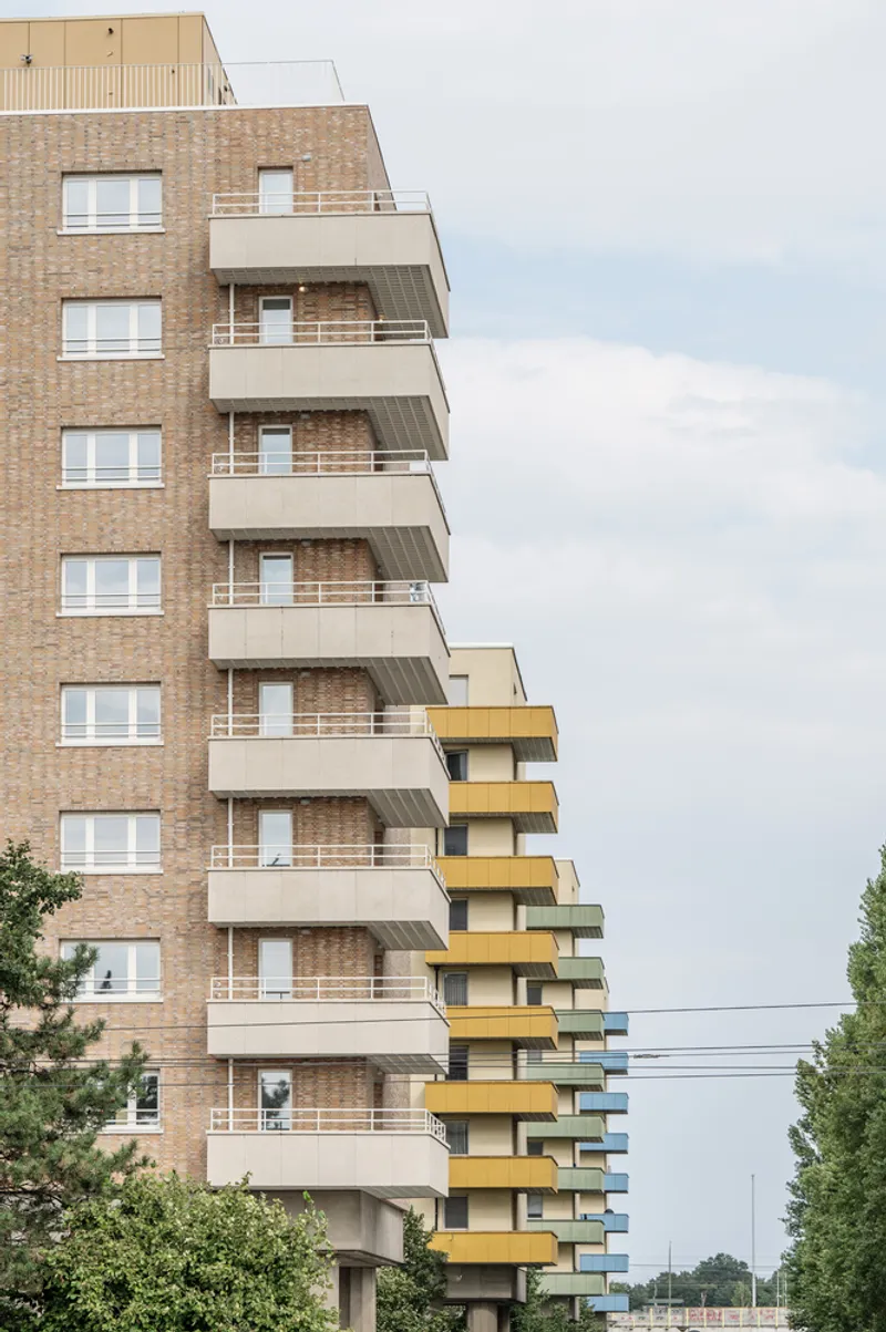 Stacked white balconies alternating with yellow corner balconies on a brick tower under overcast skies