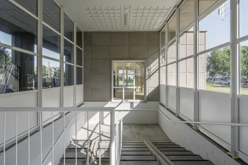 Enclosed stairwell with metal-framed glazing and concrete steps lit by afternoon sunlight