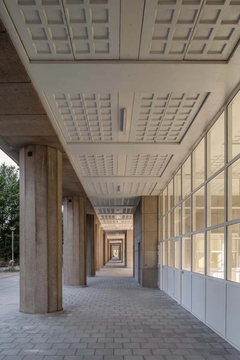 Ground-floor colonnade with coffered concrete ceiling and glazed facade alongside paved walkway