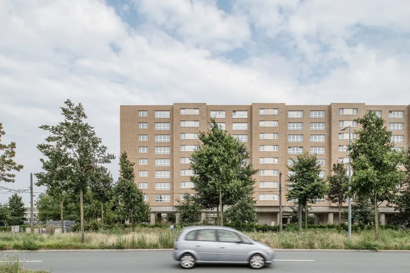 Brick residential slab with horizontal window bands viewed from the street as a car passes by