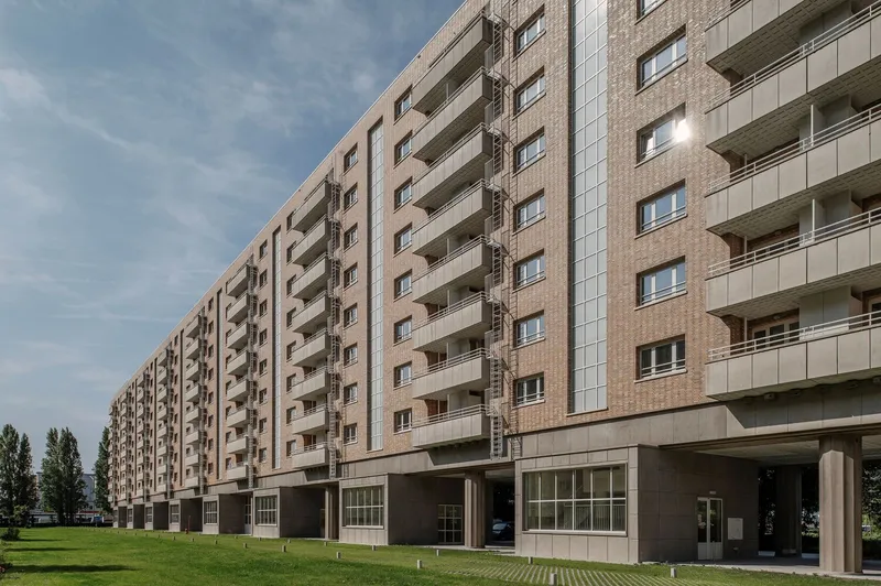 Residential block with brick facade and recessed balconies facing a lawn under cloudy skies
