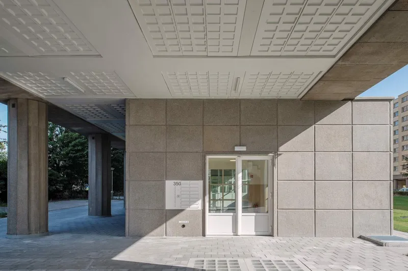 Covered entrance portico with precast concrete columns and perforated ceiling panels over paved pavers