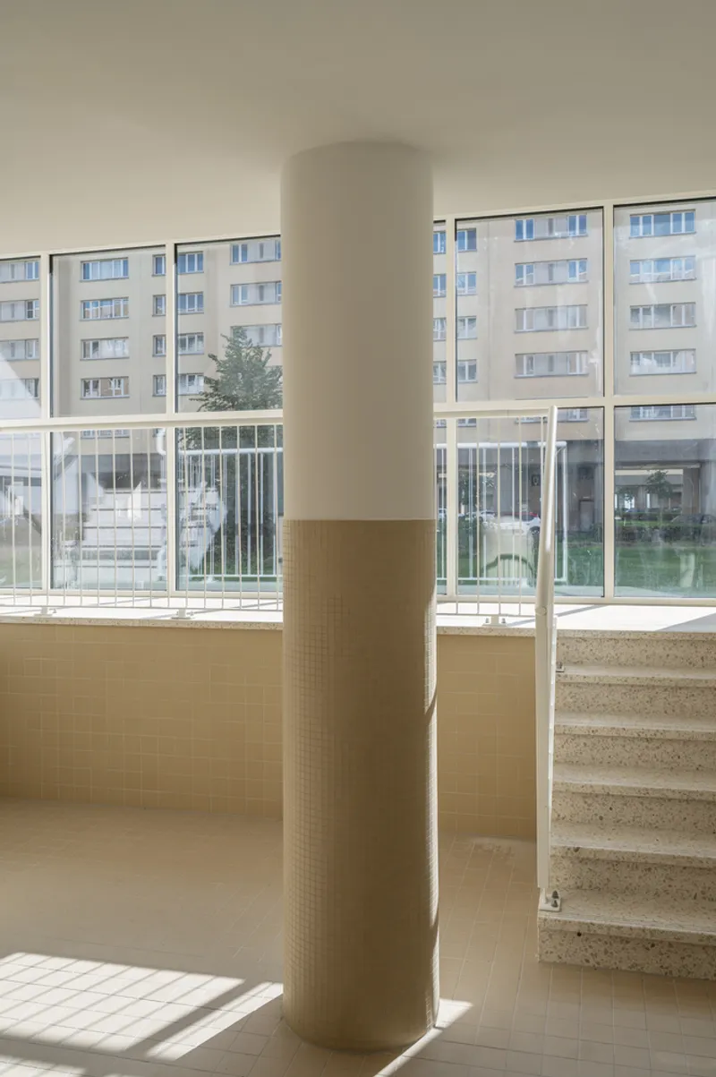 Interior lobby column wrapped in terrazzo tile beside steps and glazed courtyard view