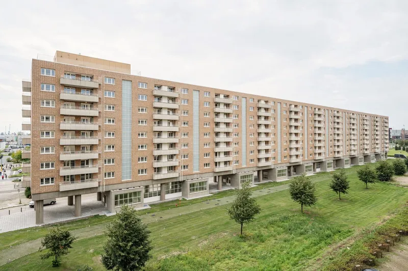 Long brick facade with recessed balconies rising above a mown lawn with young trees