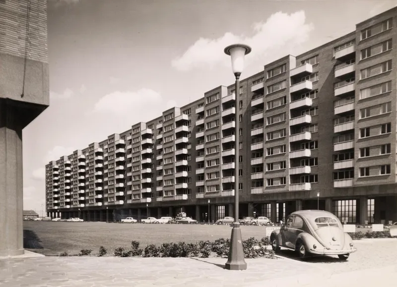 Residential slab block on pilotis with parking below and vintage car beside ornamental lamppost