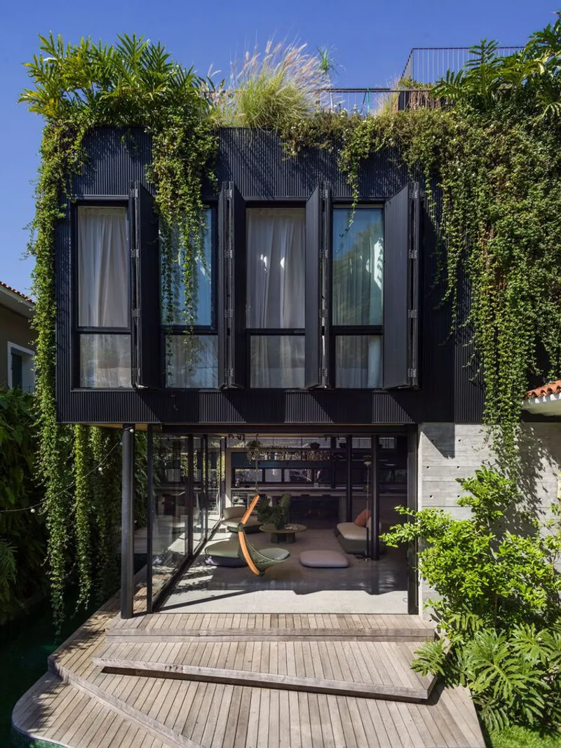 Black corrugated facade with vertical windows and cascading green wall under a clear blue sky
