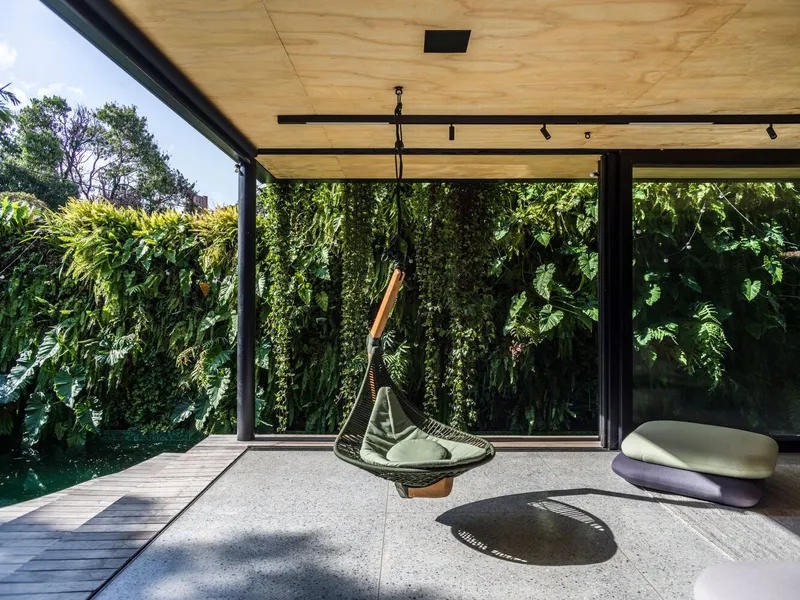 Covered terrace with plywood ceiling, black steel frame and full-height glazing opening to a vertical garden wall