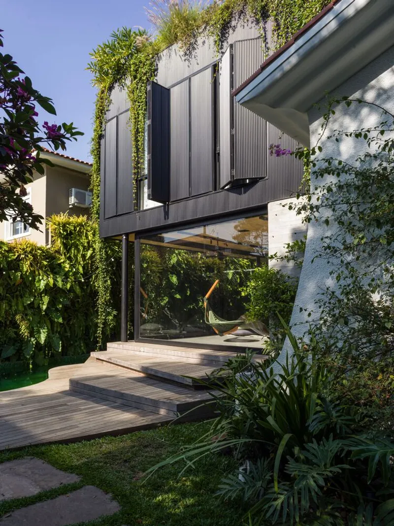 Elevated corrugated metal volume on steel columns above a timber deck with hanging chair and planted beds