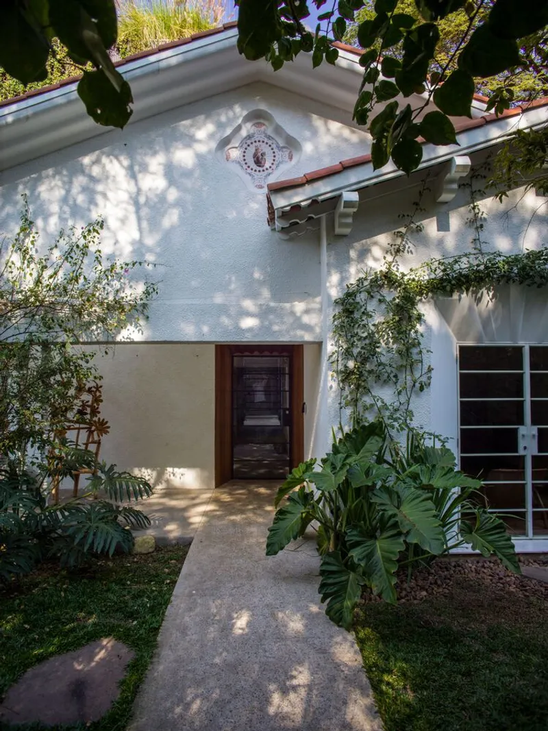 Entry facade with wooden door and carved medallion under dappled tree shade