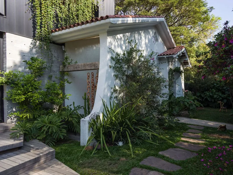 White stucco pavilion with terracotta tile roof surrounded by stepping stone path and planted beds