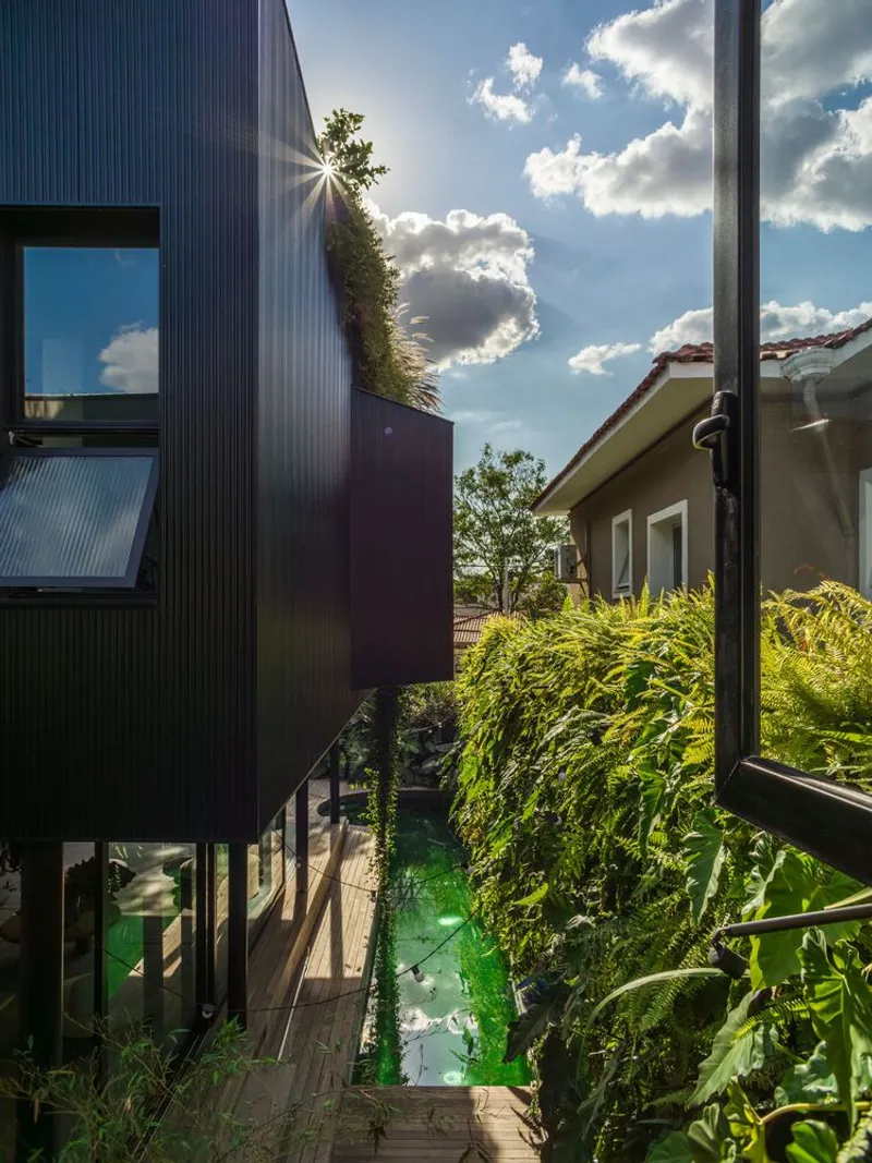 Dark corrugated metal volume with roof garden overlooking courtyard pool under afternoon sun