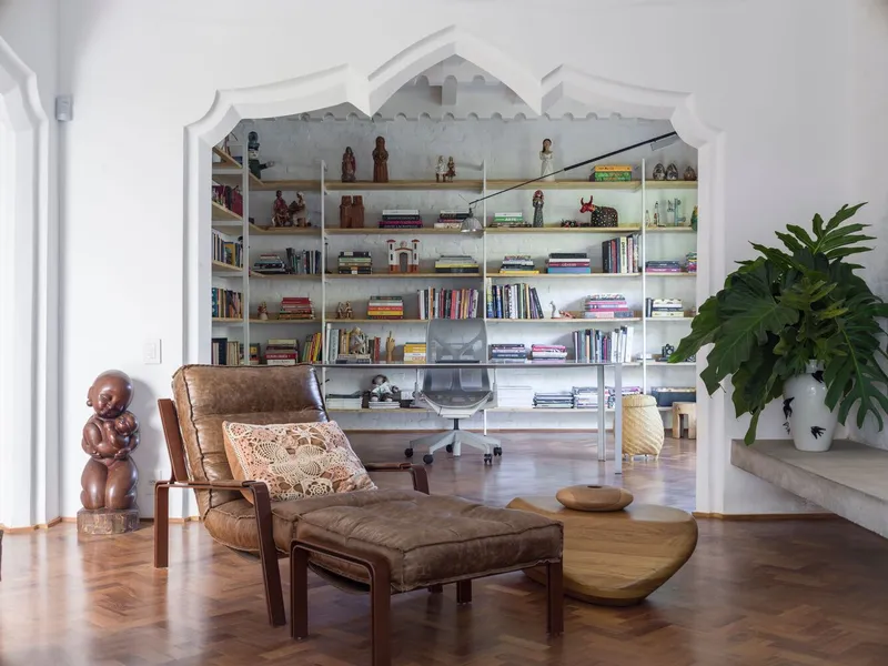 Built-in shelving with arched top frame displaying books and objects beside leather lounge chair