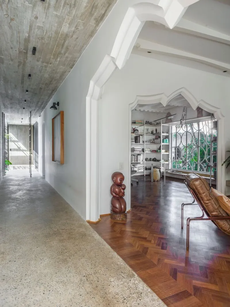 Hallway with board-formed concrete ceiling alongside herringbone wood floor leading to shelved room beyond