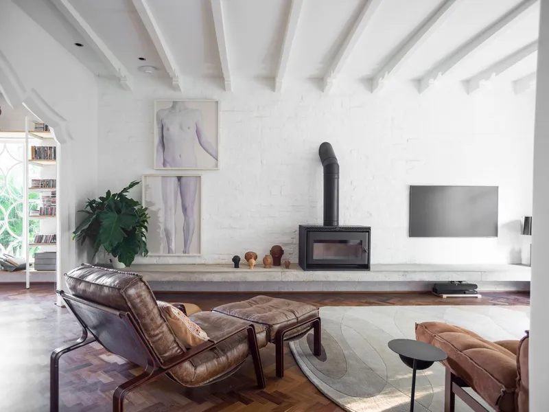 Living area with painted white brick wall, exposed ceiling beams and fireplace on concrete plinth